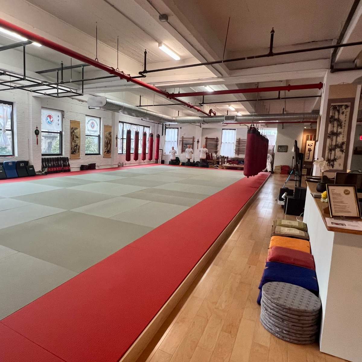 A spacious martial arts studio with light-colored mats, red borders, and a clean, minimalist design.