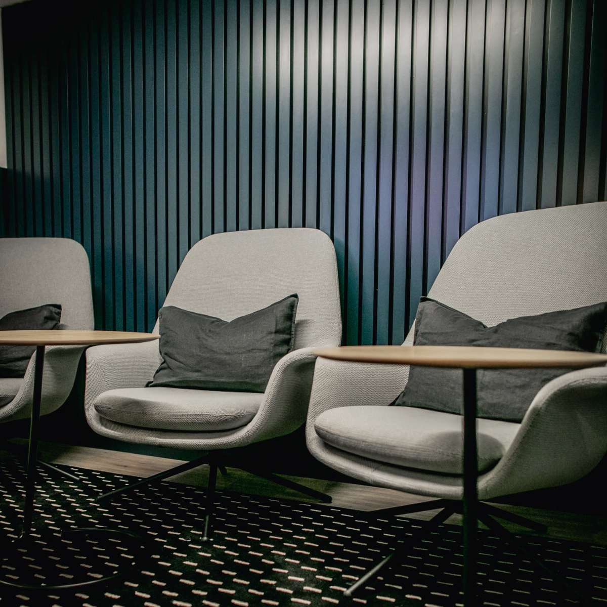 Two gray chairs with cushions are positioned in front of a wooden table, set against a striped dark wall.