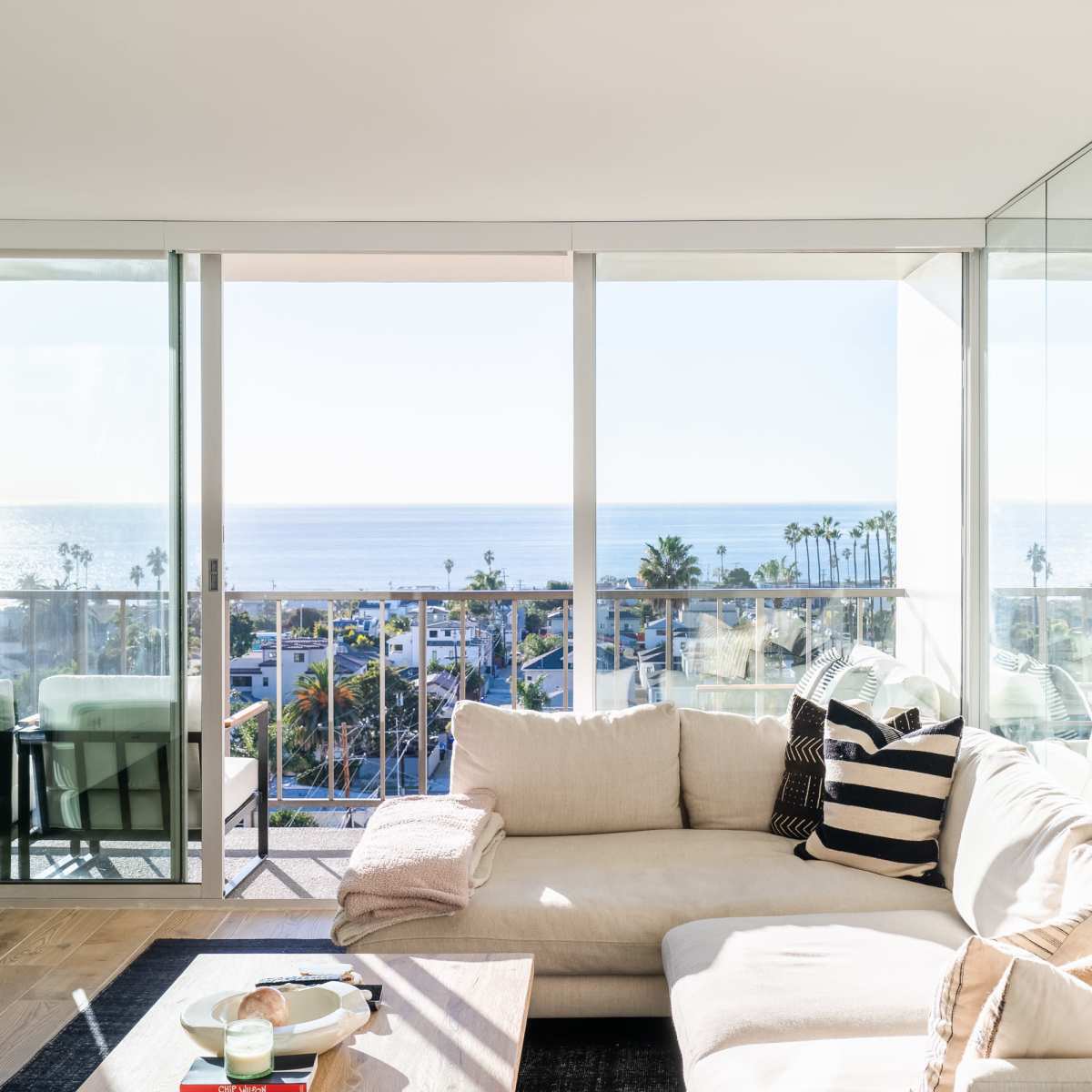 A modern living room with a large sectional couch and a coffee table overlooks a balcony with ocean views.