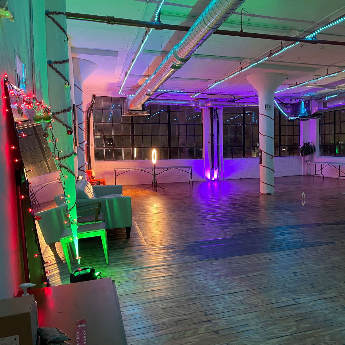 A spacious, well-lit room with wooden flooring, featuring colorful lighting and decorative elements along the walls and columns.
