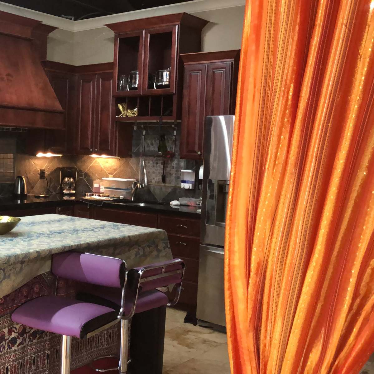 A modern kitchen with dark wooden cabinets, a central island covered by a tablecloth, and a variety of kitchen appliances.