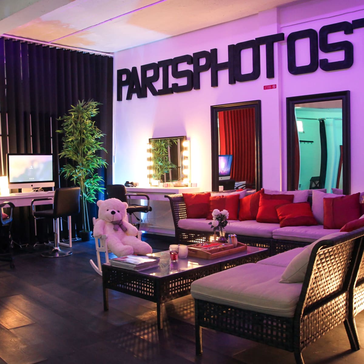 A modern photography studio with a lounge area featuring a sectional sofa, decorative pillows, and a large sign reading "PARISPHOTOST."