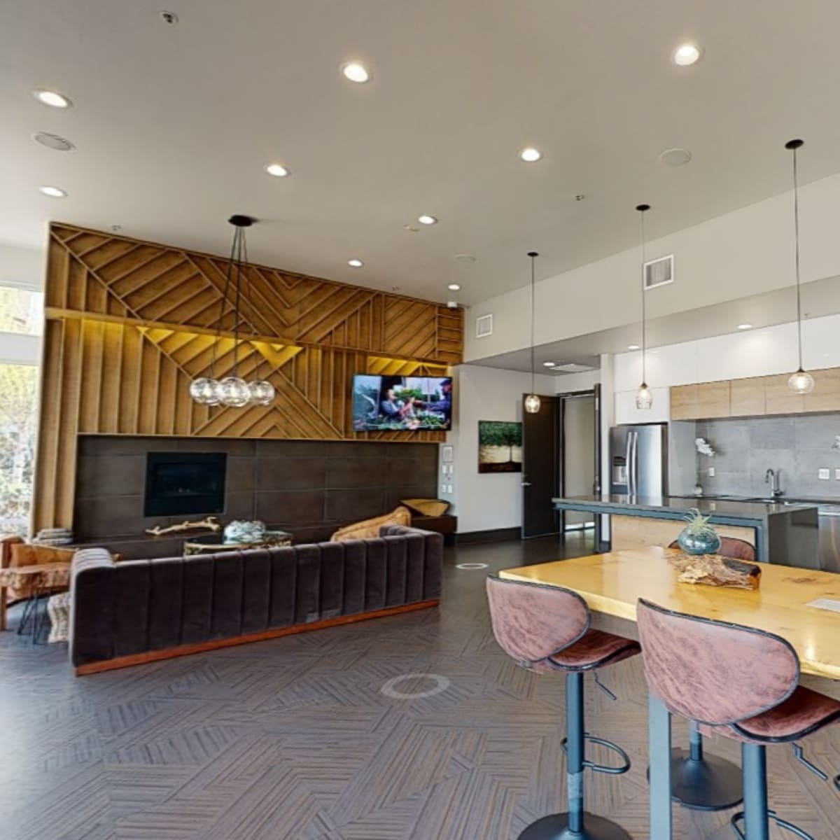 The scene features a modern, open-concept lounge area with a kitchen, dining table, and comfortable seating arranged around a television.