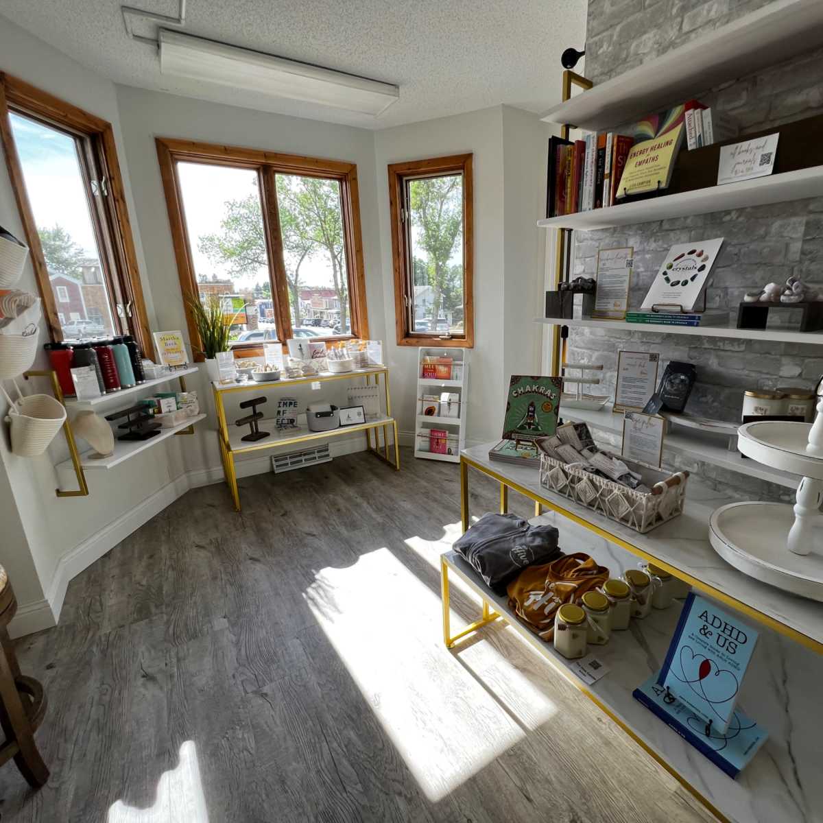 A bright interior of a boutique with wooden shelves displaying various products and a corner window allowing natural light to enter.