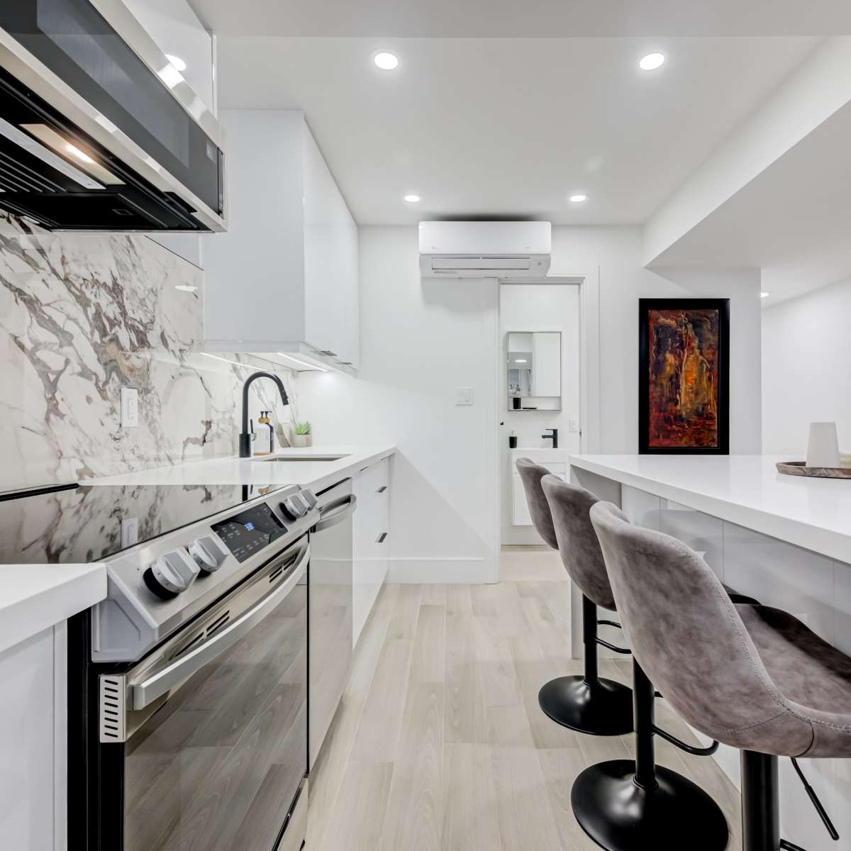 A modern kitchen features a marble backsplash, stainless steel appliances, and a white island with bar stools.
