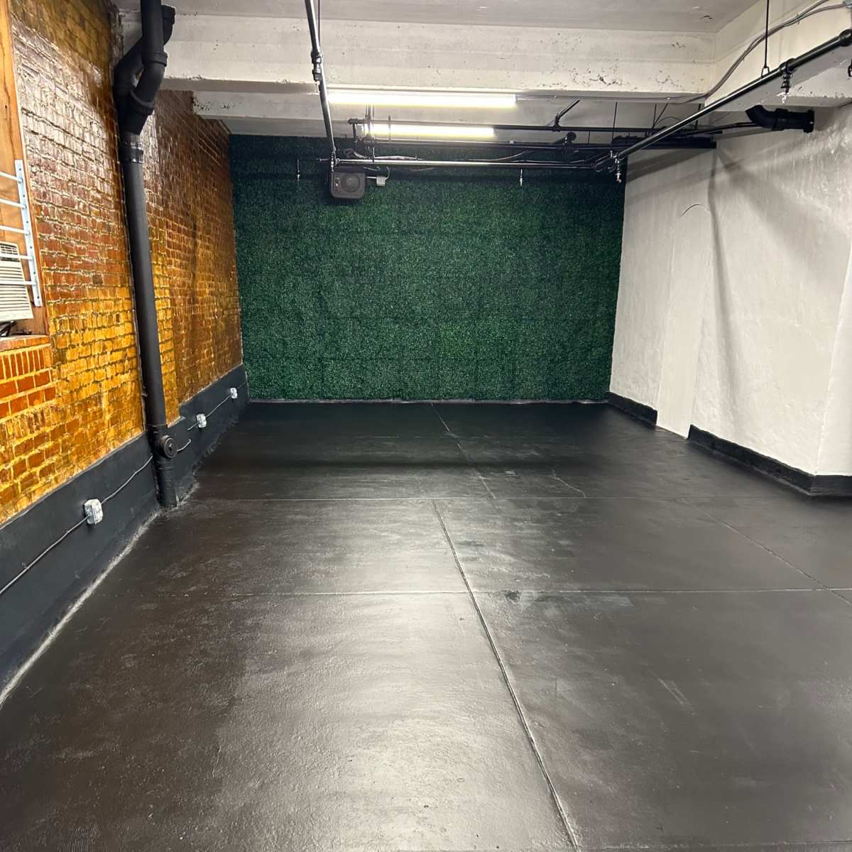 An empty, polished black floor in a room with brick walls on one side and a green fabric backdrop on the opposite wall.