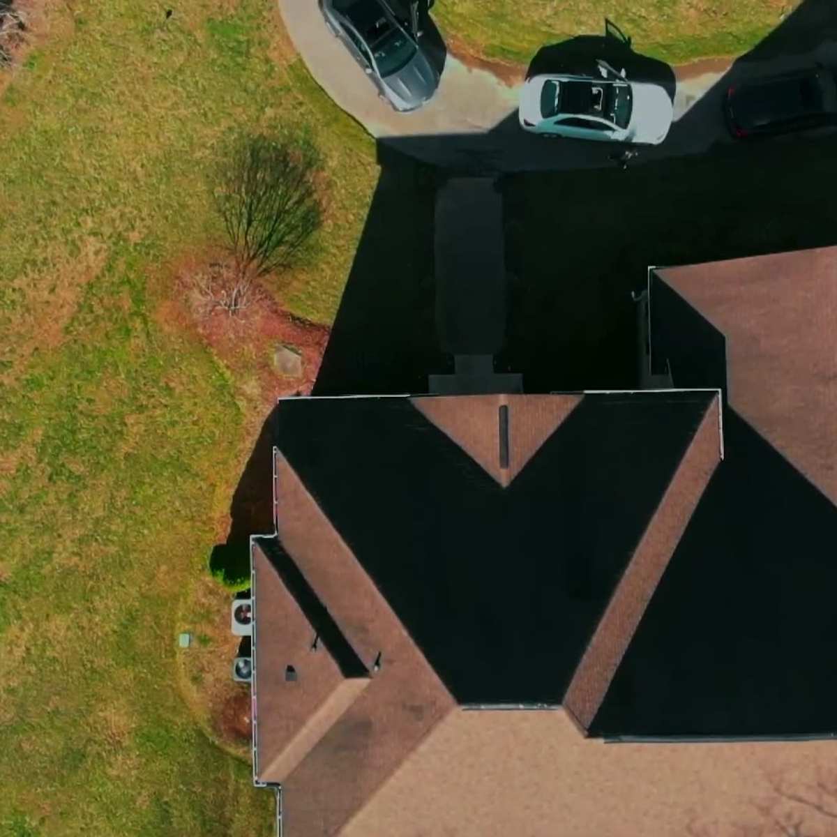 An aerial view of a residential property with several cars parked in a driveway and a large expanse of grass surrounding the house.
