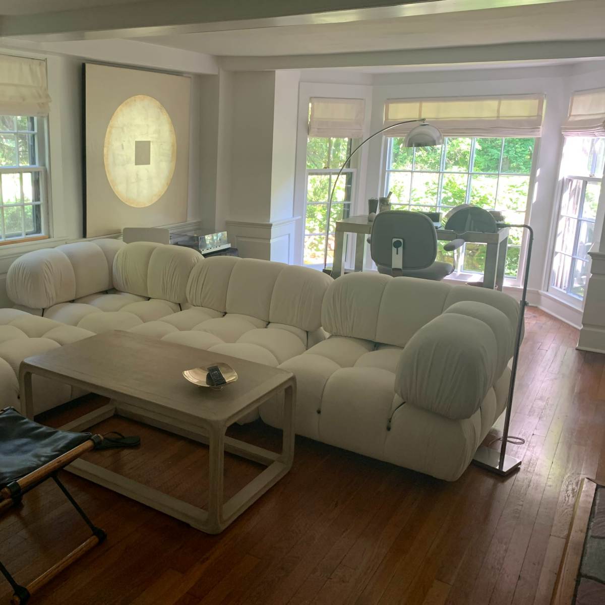 A modern living room with a white sectional sofa, a wooden coffee table, and large windows allowing natural light to enter.