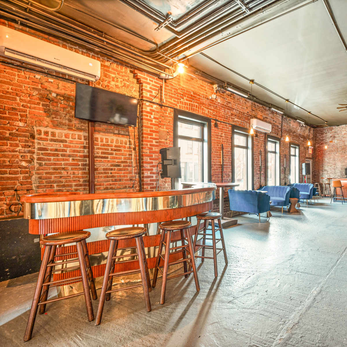 An interior of a bar with exposed brick walls, a wooden bar counter, and various seating arrangements.