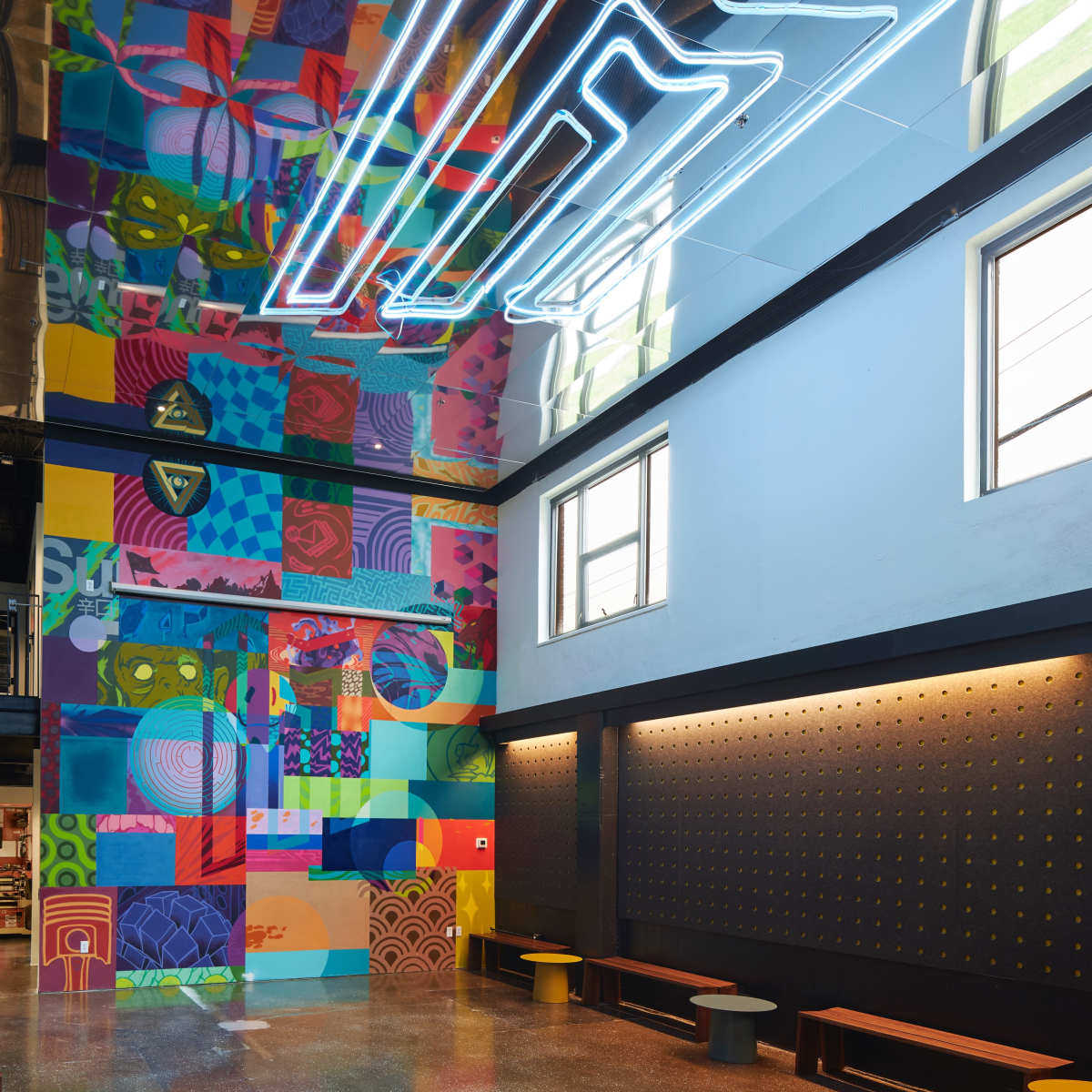 A modern interior space with a colorful mural on one wall and a neon sign on the ceiling.