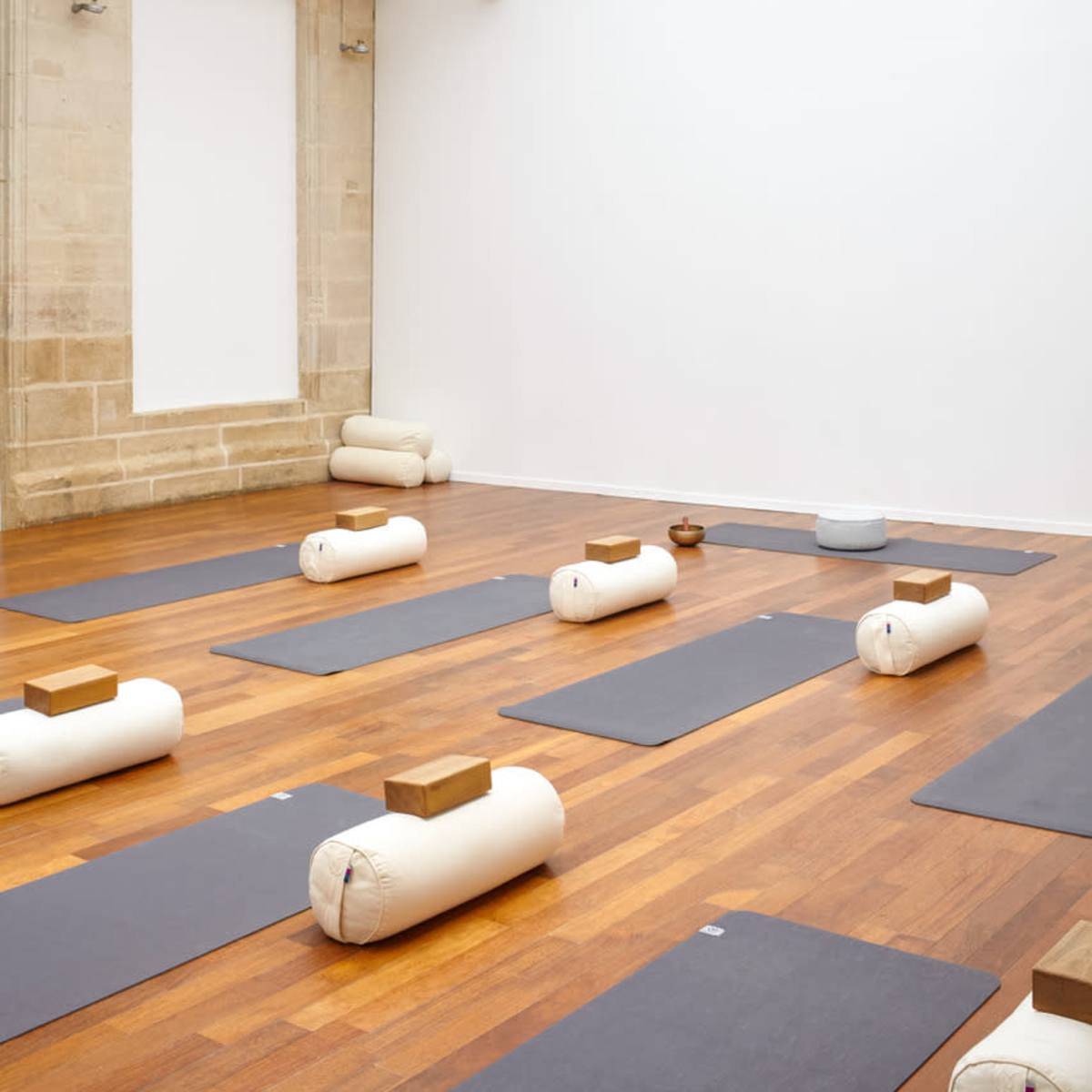 A spacious yoga studio with wooden flooring, several yoga mats neatly arranged, and natural light streaming through a glass roof.