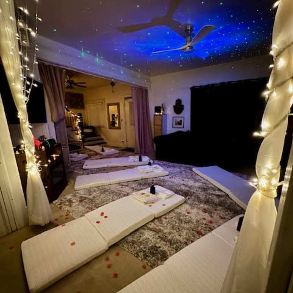 A room set up for relaxation with several white mats on a rug, surrounded by soft lighting and a ceiling decorated with star-like projections.