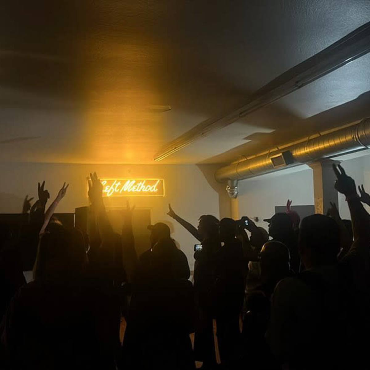 A crowd of people raises their hands in front of a brightly lit sign in a dimly lit room.