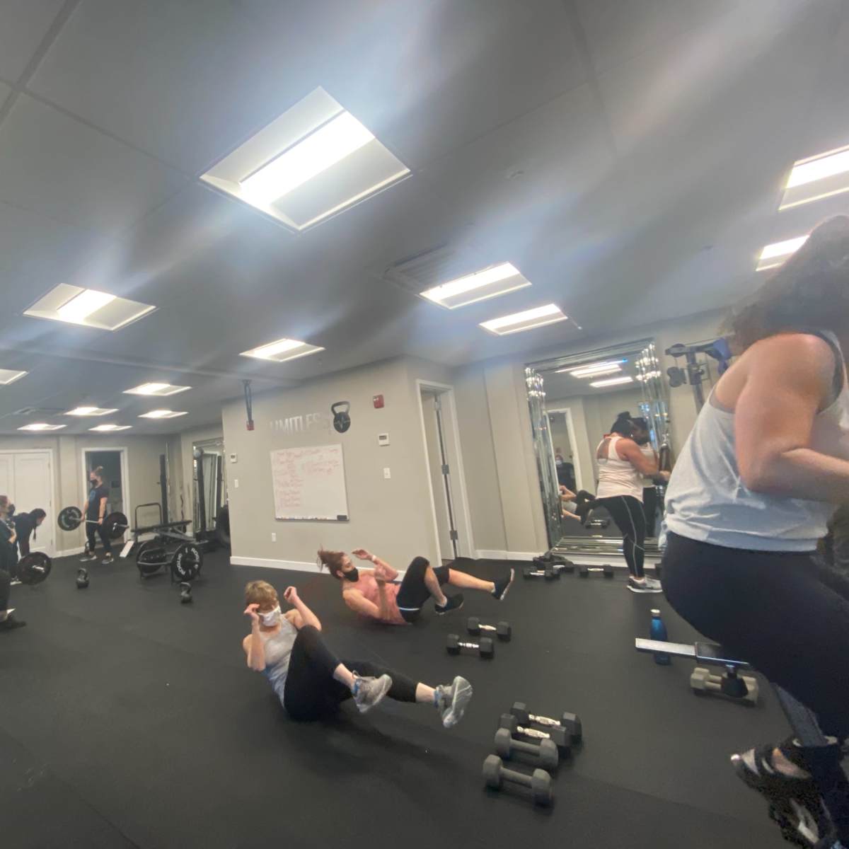 A group of people performs various workout exercises in a fitness studio equipped with weights and exercise mats.