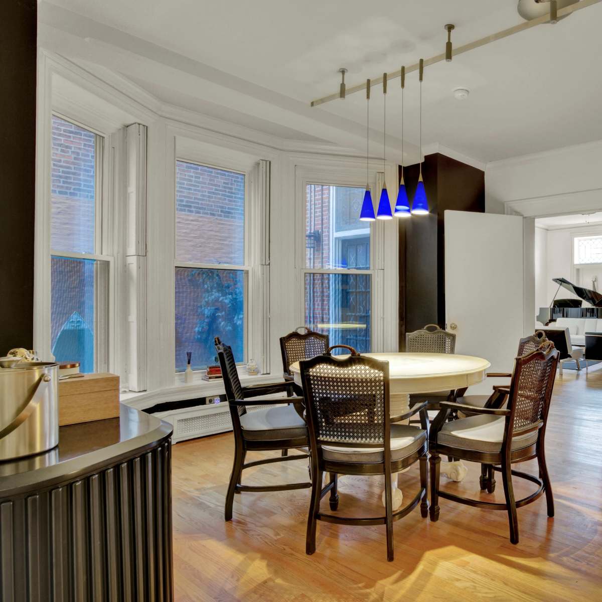 A dining area features a round table surrounded by wooden chairs and is illuminated by three pendant lights.