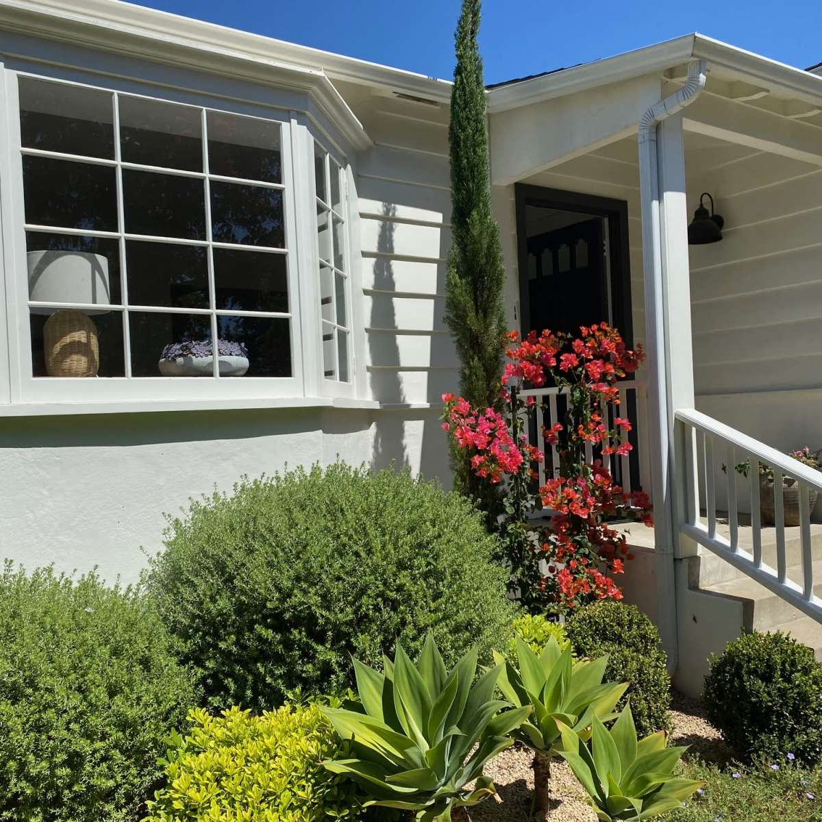 A light-colored house features a decorative front garden with colorful flowers and neatly trimmed shrubs.