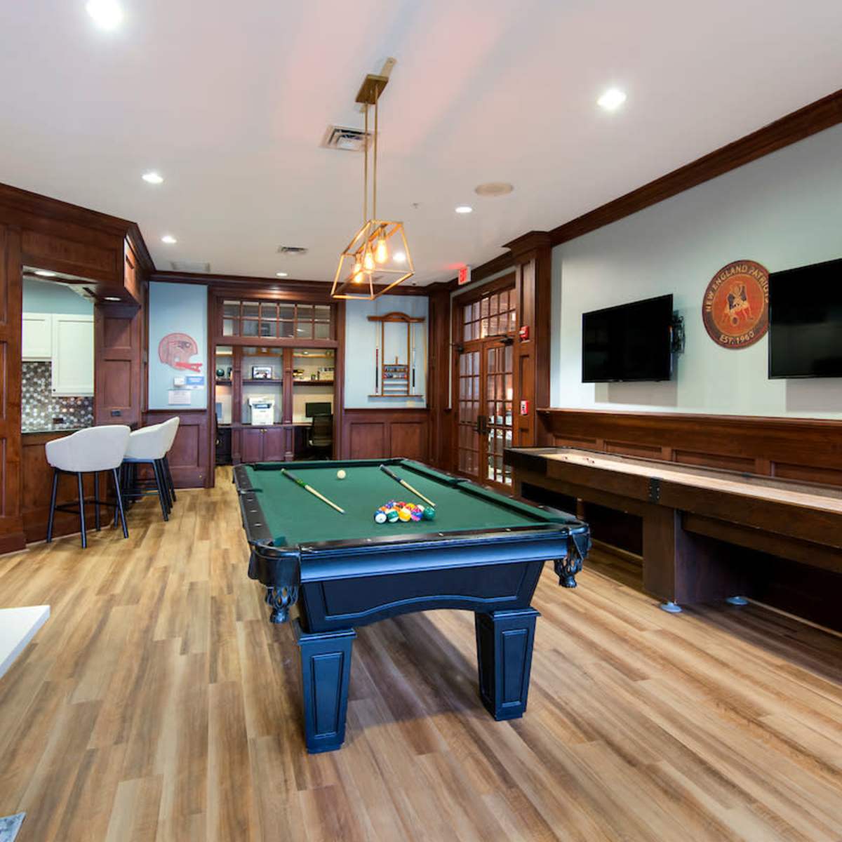 A game room featuring a pool table, wood-paneled walls, and a kitchenette area with modern appliances.