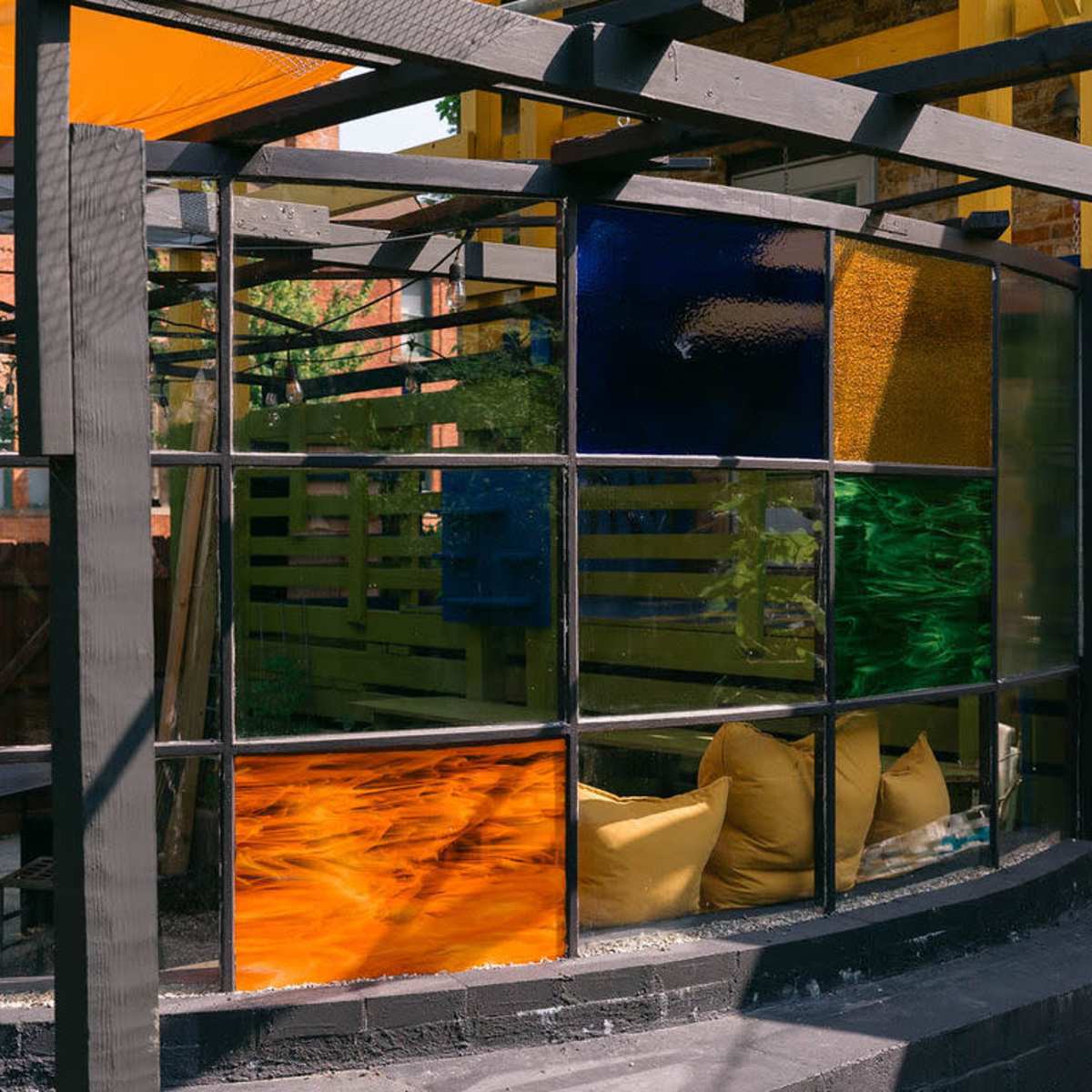 A segmented glass wall featuring panels of various colors, surrounded by a landscaping of greenery and outdoor seating.