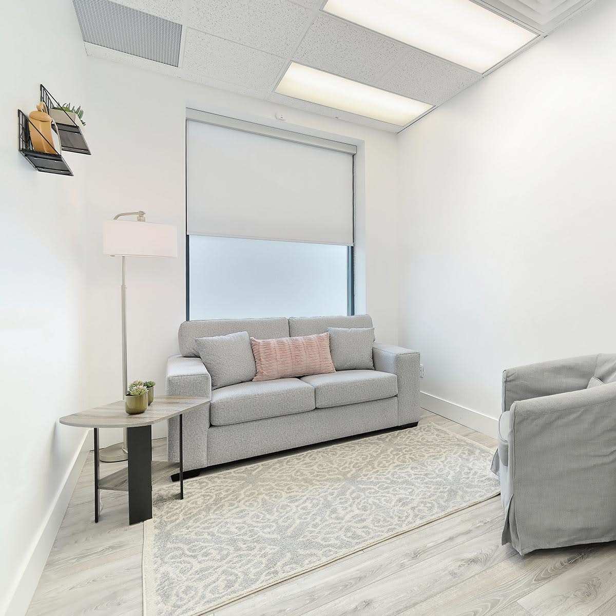 A small, neatly arranged office space with a couch, a side table, a desk, and a chair.