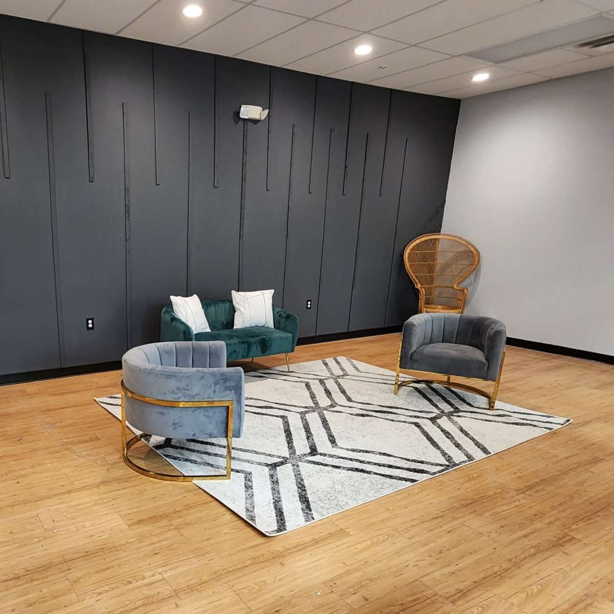 A stylish interior space featuring a green velvet sofa, a blue upholstered chair, and a large mirror against a geometric-patterned rug on a wooden floor.