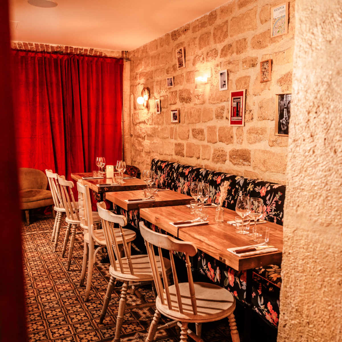 A cozy dining area with wooden tables, floral upholstered seating, and a stone wall adorned with framed photos.