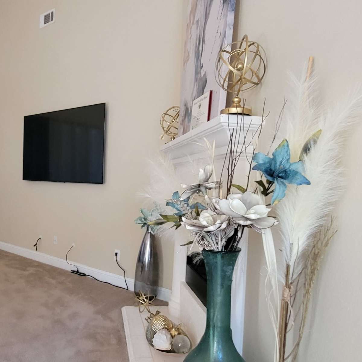 A living room with a television mounted on the wall, a decorative fireplace, and a vase with flowers on a table beside a dark leather sofa.