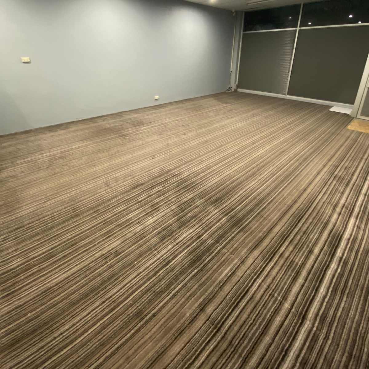 A vacant room with gray walls, a carpeted floor featuring stripes, and lighting from overhead ceiling fixtures.