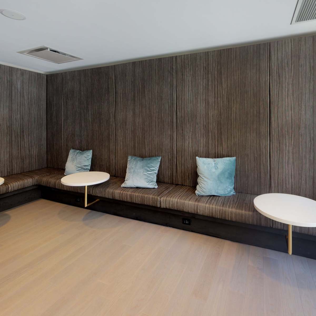 A modern lounge area featuring a low, cushioned seating arrangement with light blue pillows and small round tables.