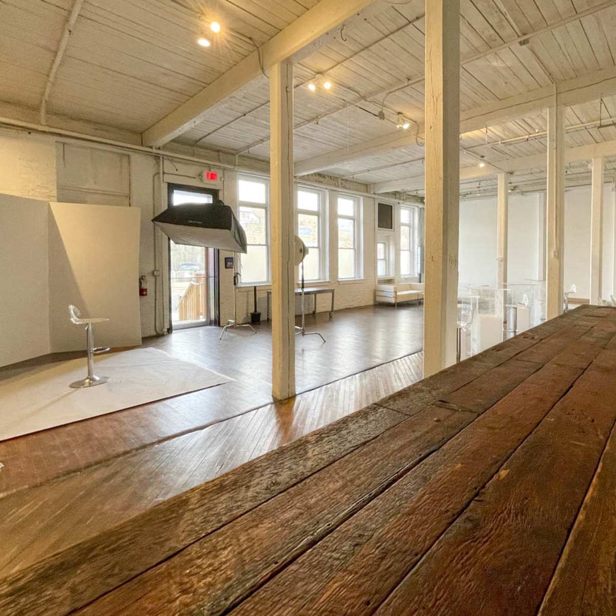 A spacious studio with wooden flooring, large windows, and a bar-like counter in the foreground.