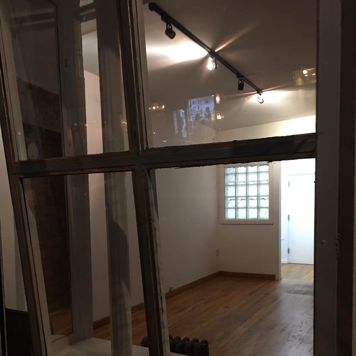 A view through a window into a sparsely furnished room with hardwood floors and glass block walls.