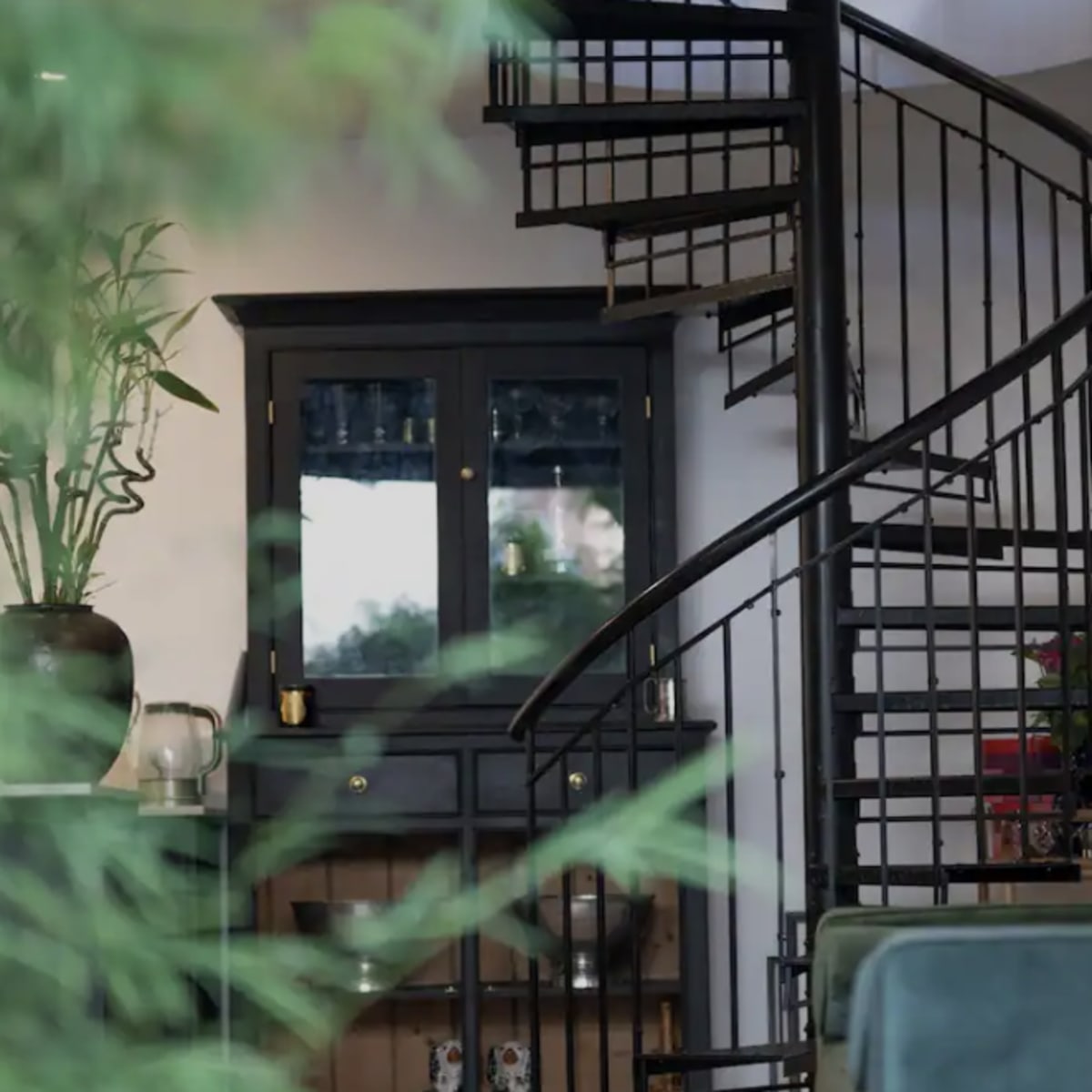 A spiral staircase leading to a second level, with a dark cabinet and green plants visible in the surrounding area.