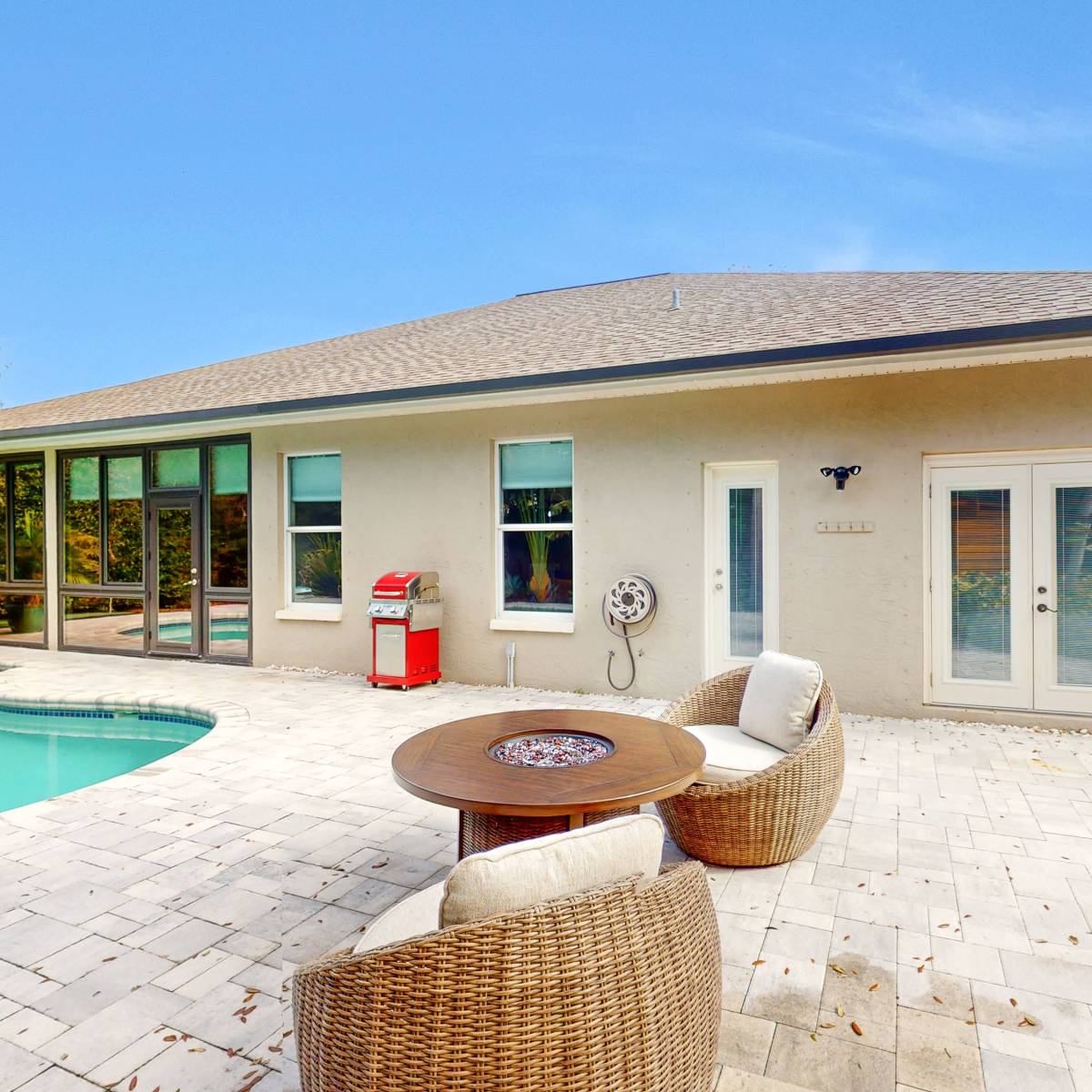 A modern house features a patio with a pool, outdoor seating, and a small garden area.