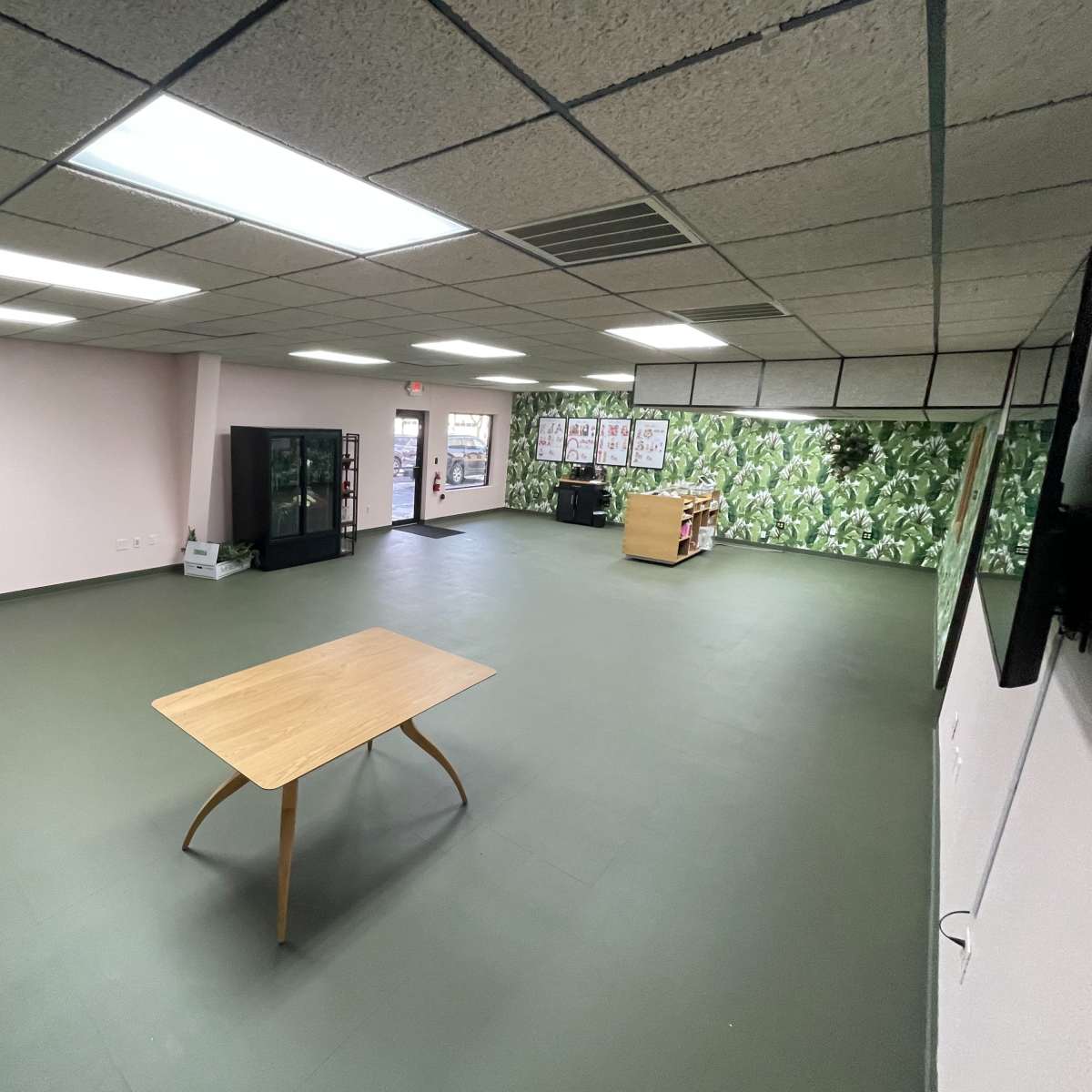 A spacious, empty room with a wooden table in the center, surrounding walls painted in light colors, and one wall featuring a green patterned mural.