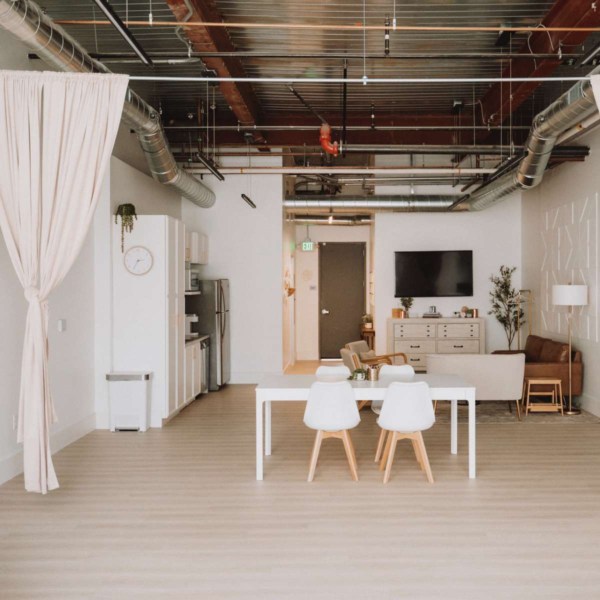 A spacious, modern interior with a dining table and chairs in the foreground, light-colored flooring, and a kitchen area in the background.