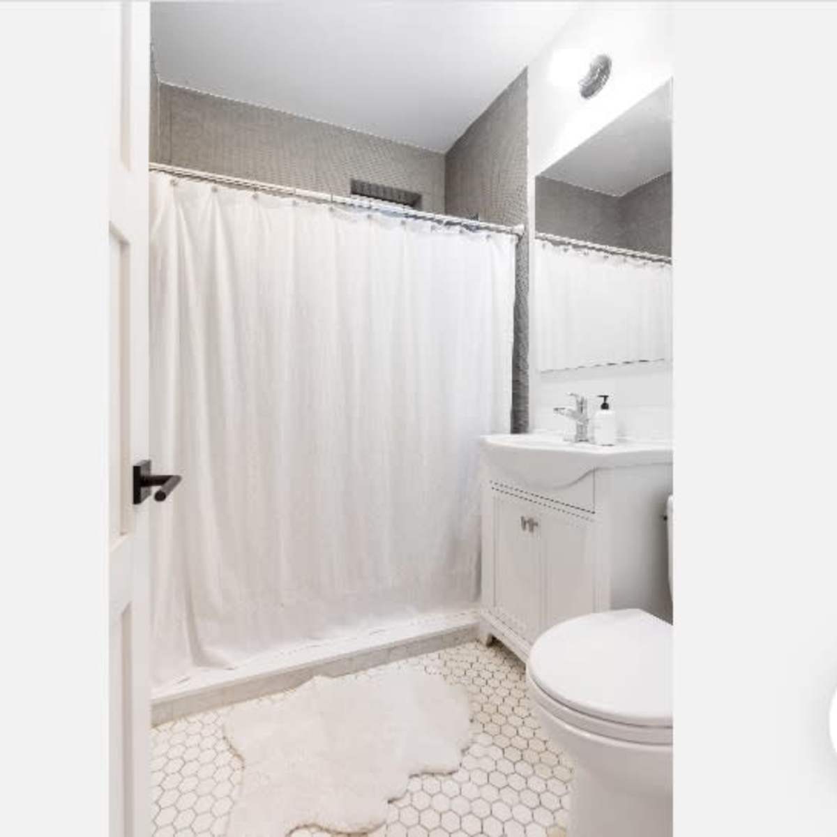 A bathroom with a shower curtain, a white sink, a toilet, and hexagonal tiles on the floor.