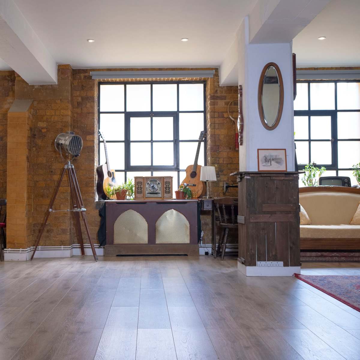 A spacious interior with wooden flooring, large windows, and vintage decor, including a swing, guitars, and plants.