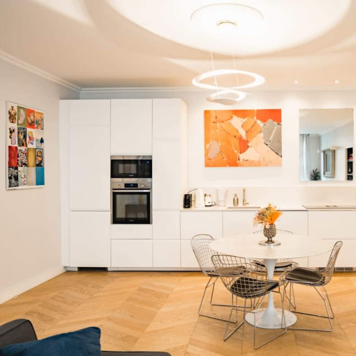 A modern kitchen and dining area featuring a round white table with metal chairs, a sleek white cabinetry setup, and artwork displayed on the walls.