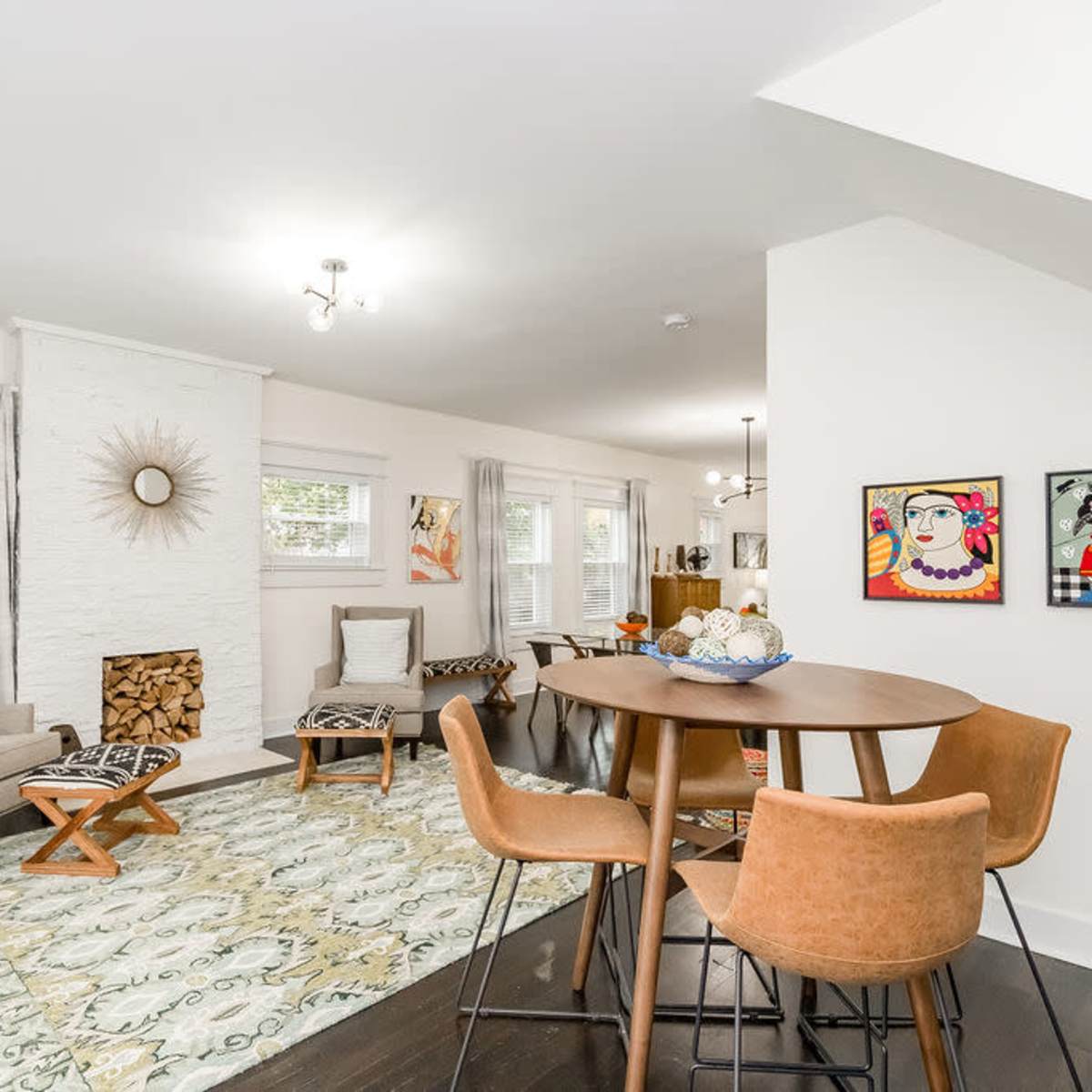 A bright and modern living space featuring a dining table with brown chairs, a cozy seating area, and a white-washed fireplace adorned with artwork and decorative items.