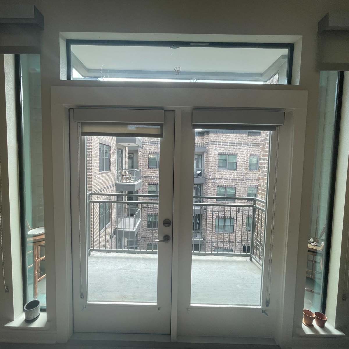 A set of double doors leading to a balcony with a view of an adjacent brick building.