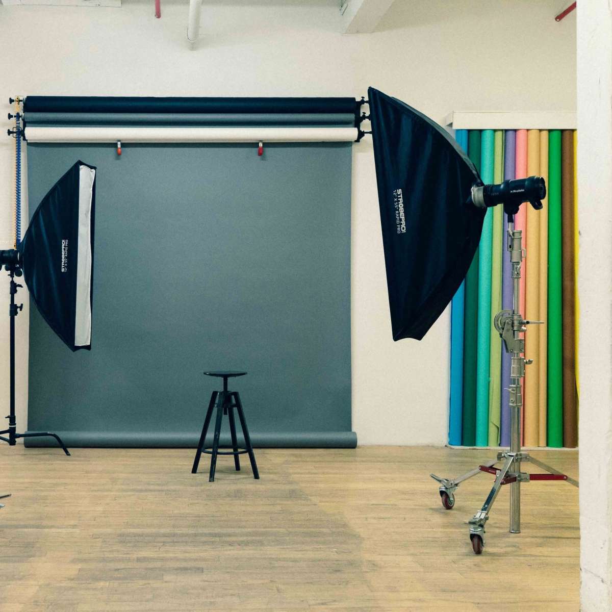 A photography studio with a gray backdrop, a stool in the center, and two softbox light setups positioned on either side.