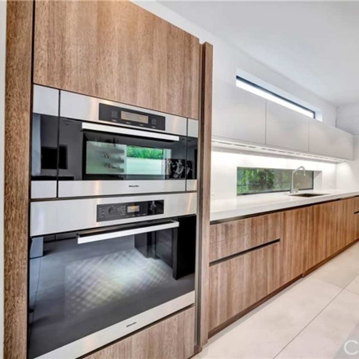 A modern kitchen with wooden cabinetry, stainless steel appliances, and a white countertop.