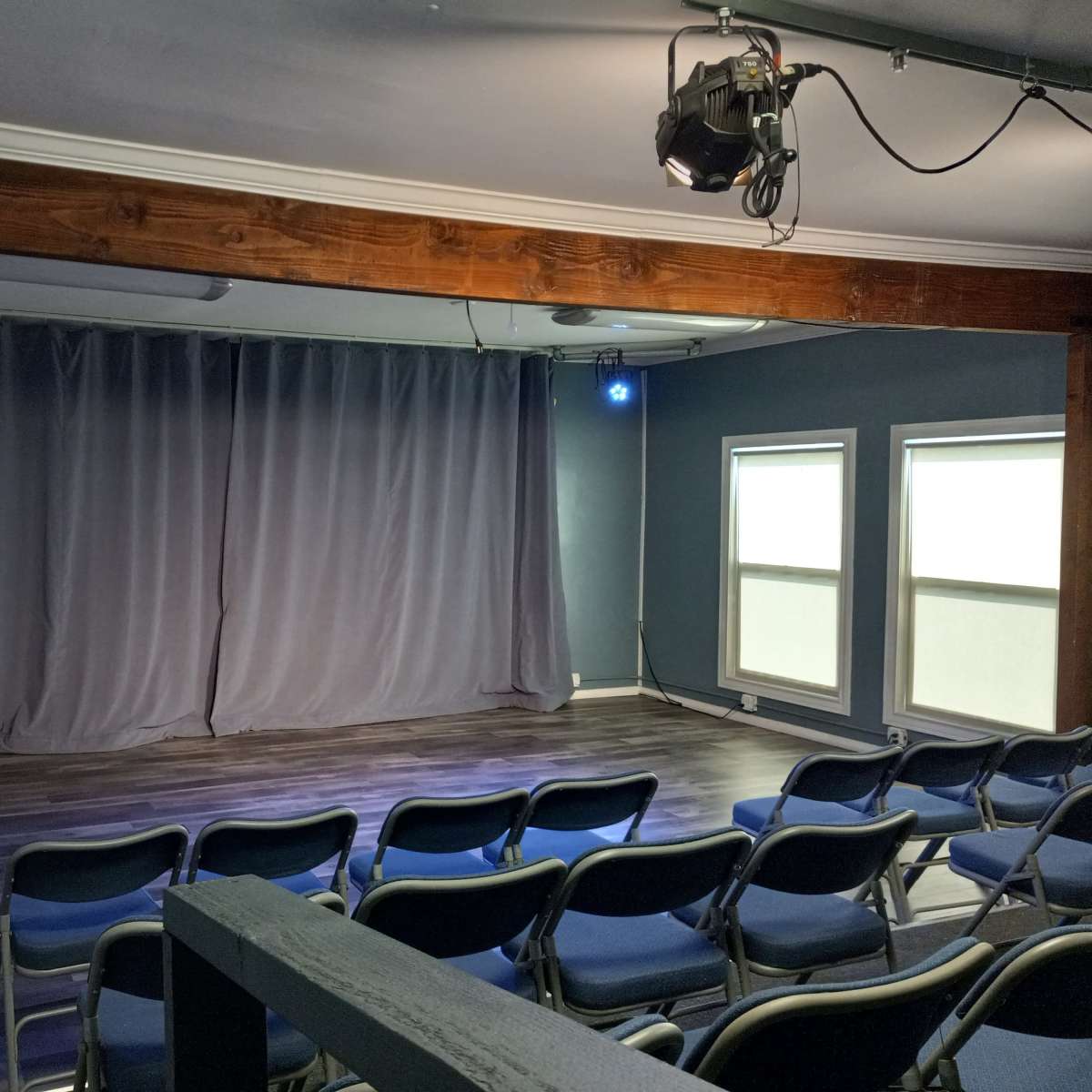 A small theater space with gray curtains, blue lights, and rows of blue chairs facing the stage.