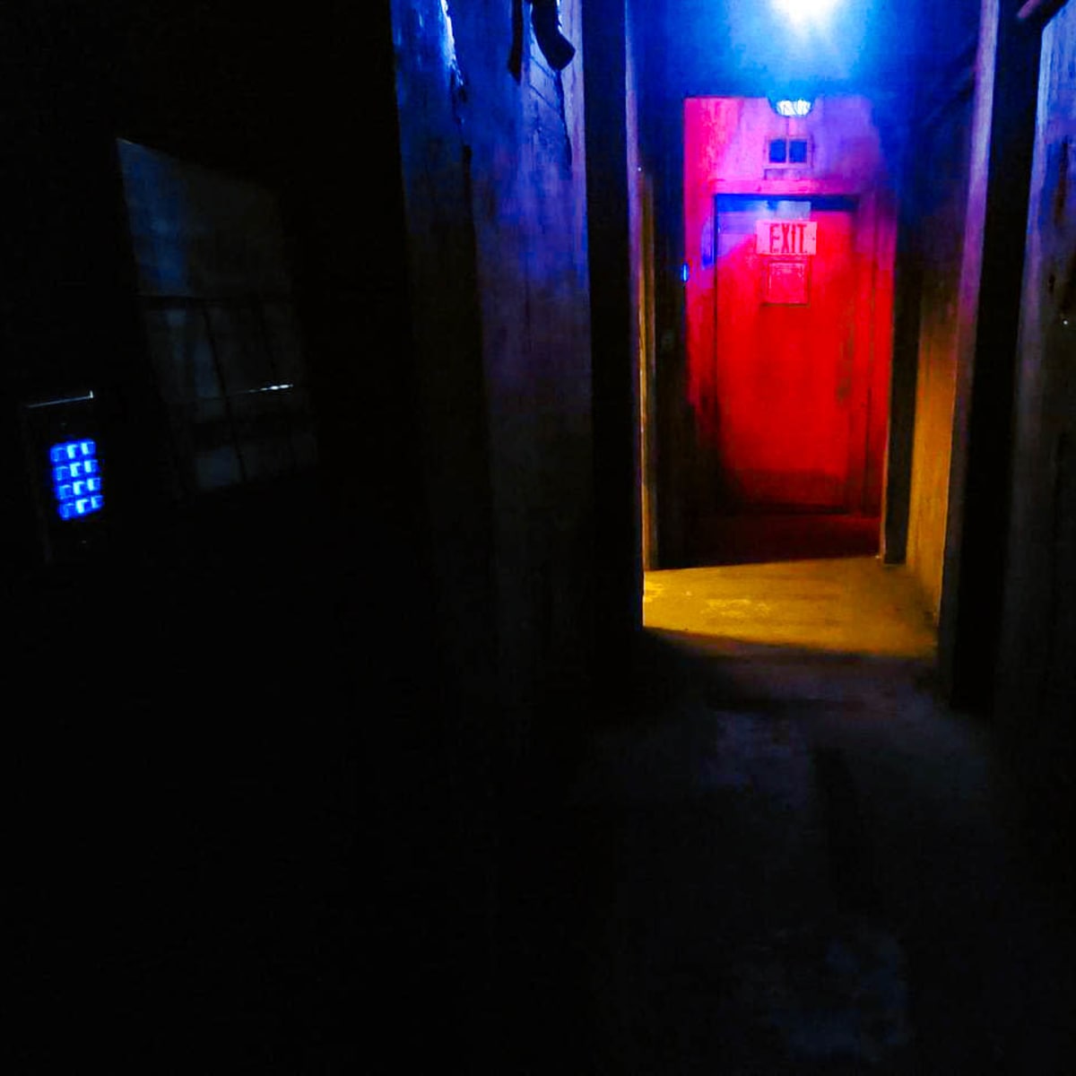 A dimly lit hallway with walls painted in dark colors, illuminated by red and blue lights at the far end.
