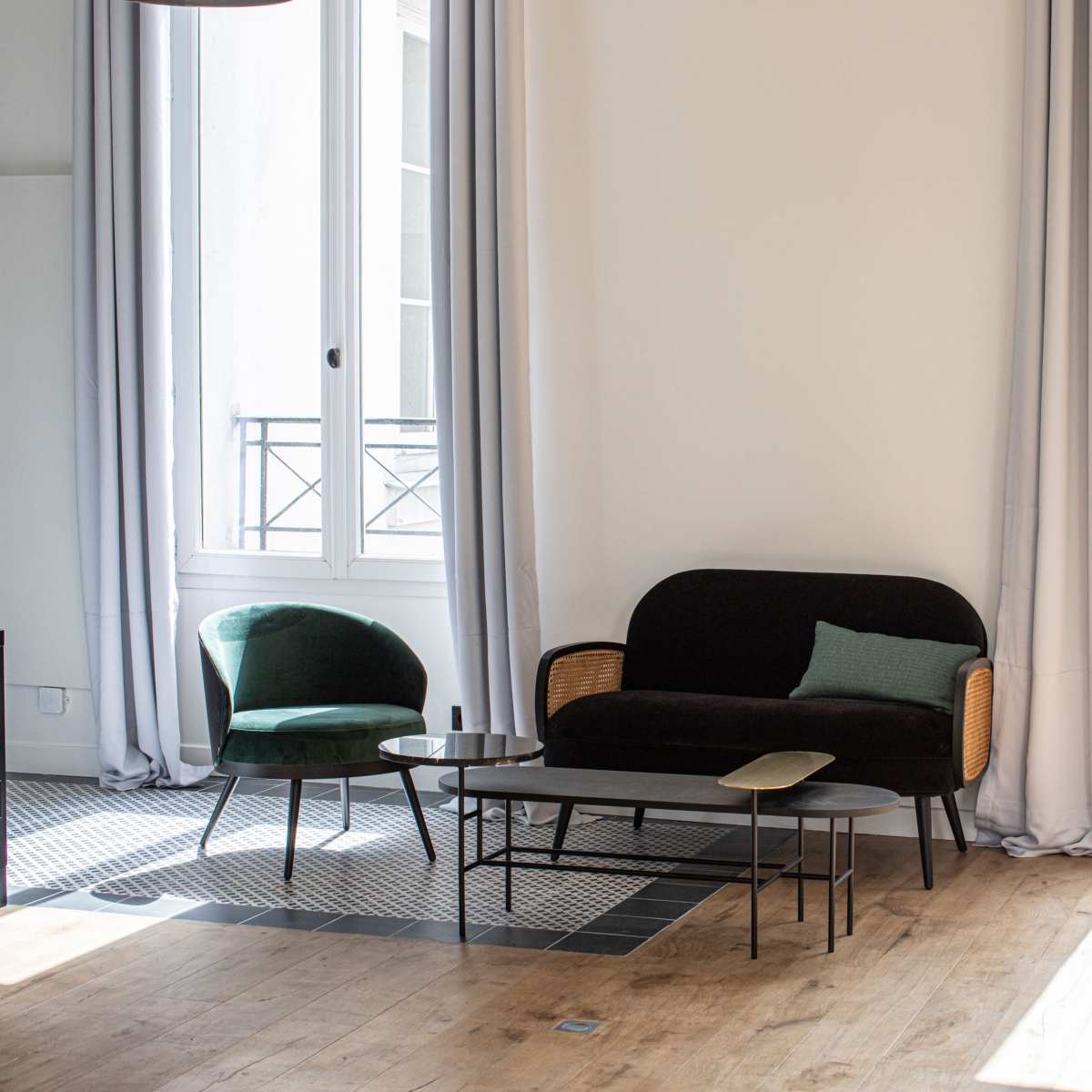 A minimalist living room with a black sofa, two armchairs, and a coffee table near large windows.