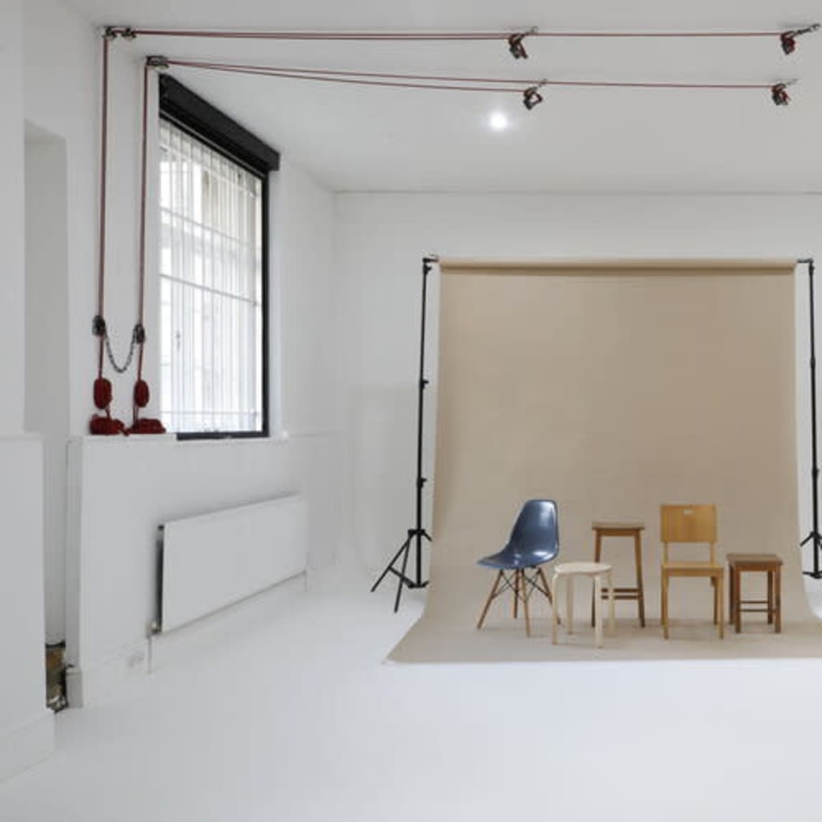 A minimalist studio space with three chairs arranged in front of a beige backdrop.