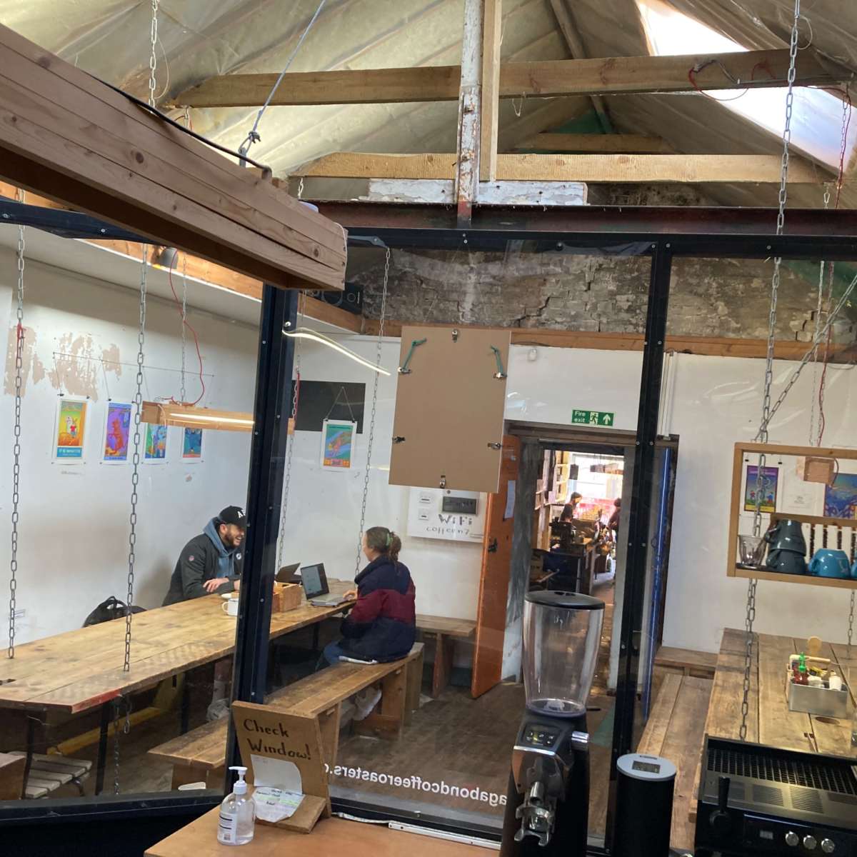 A cozy café with wooden tables and a large open space, featuring patrons sitting at tables and a serving counter with coffee equipment.