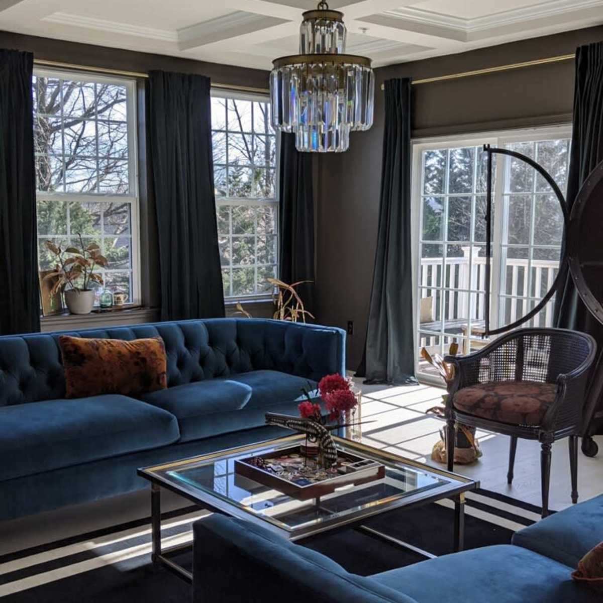 A bright living room features blue sofas, a glass coffee table, and a modern chandelier, with large windows letting in ample natural light.