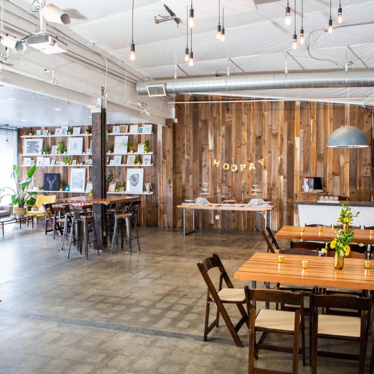 A spacious indoor venue with wooden decor, long tables arranged for dining, and a small service area against a rustic wooden wall.