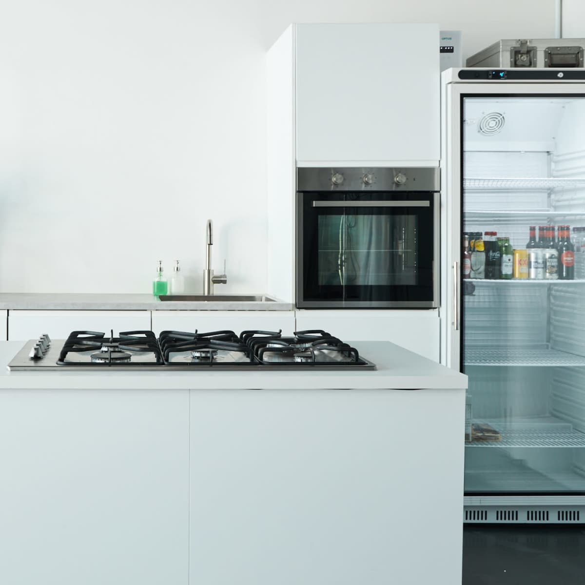 A modern kitchen with a gas stove island, a built-in oven, a refrigerator, and a potted plant on a countertop.