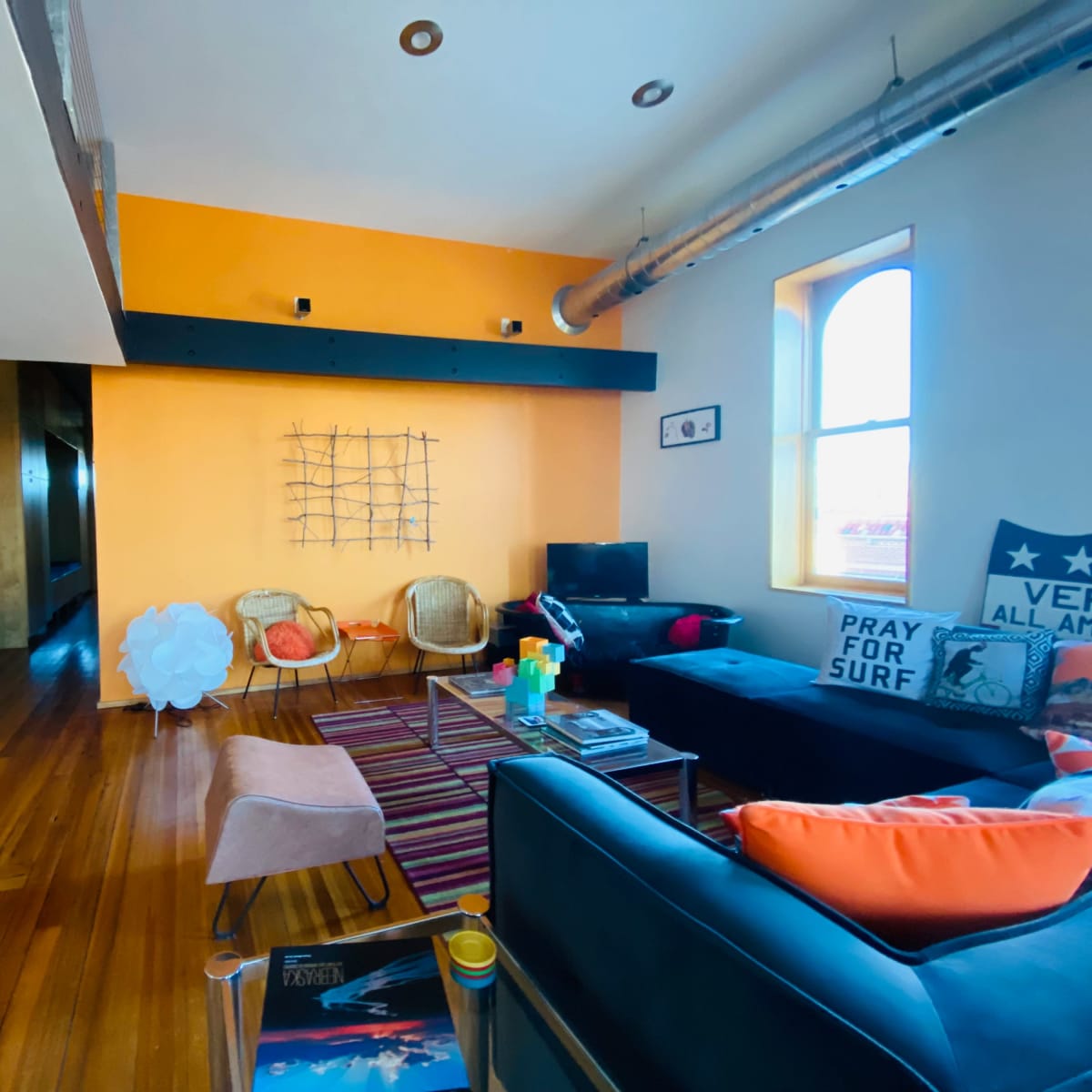 A modern living space with orange walls, a combination of seating options, and a kitchen area in the background.